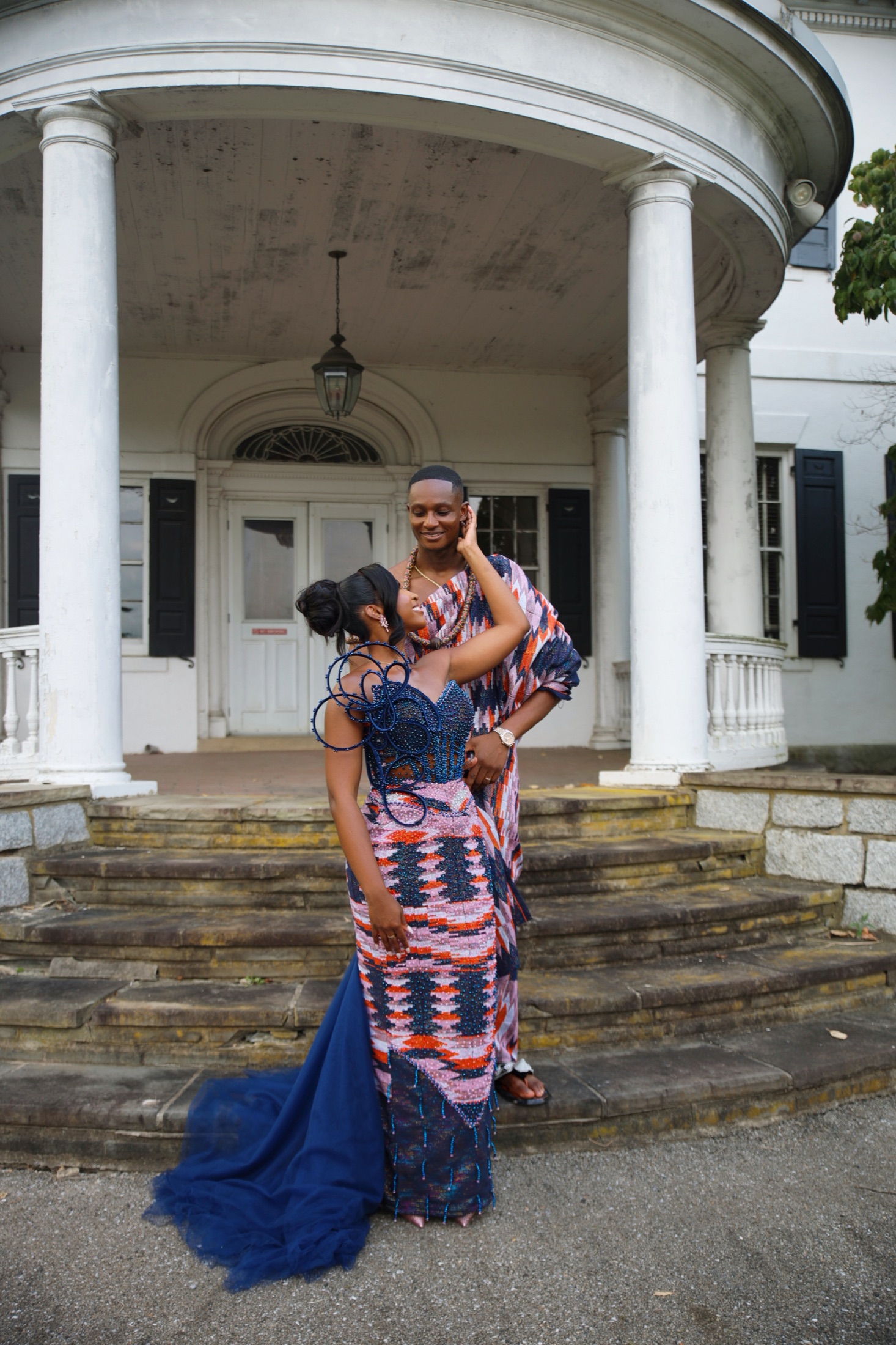 A couple in coordinated kente attire with their party on grand steps